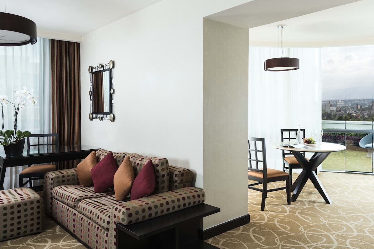 A modern living room with a sofa, a dining table with chairs, and a view of the city through large windows.