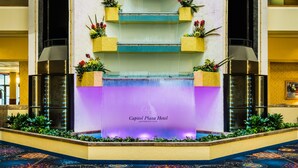 Un hall d’hôtel agrémenté d’une fontaine centrale, de jardinières fleuries et d’une enseigne indiquant le Capitol Plaza Hotel, situé à Jefferson City.