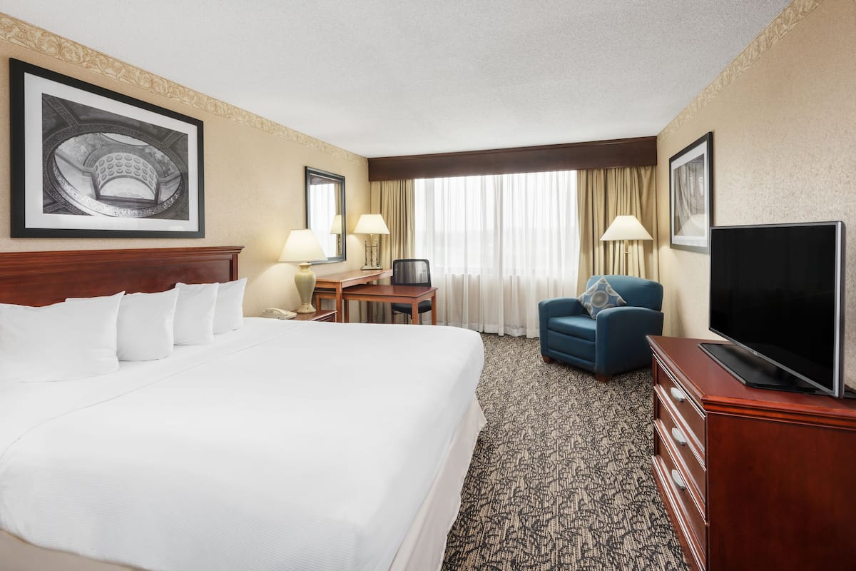 A hotel room with a large bed, a desk with a chair, a television, and a blue armchair.