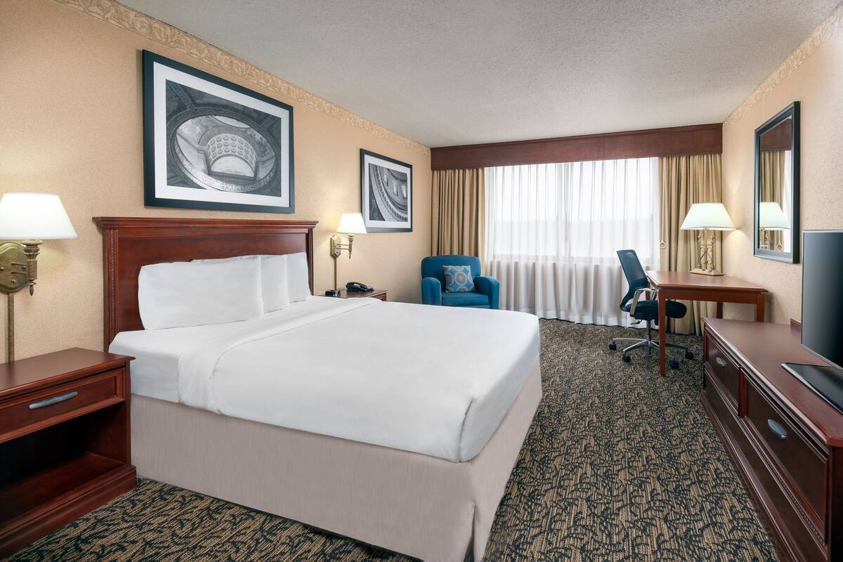 A hotel room with a large bed, a desk, a chair, and a television.