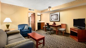 Une chambre d’hôtel avec un canapé, une petite table, un bureau avec une chaise, une télévision et un tableau encadré au mur.