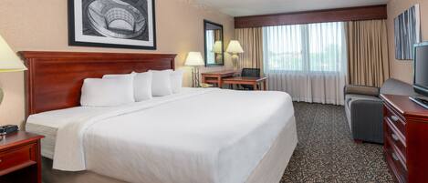 A hotel room with a large bed, a desk, a chair, and a television.