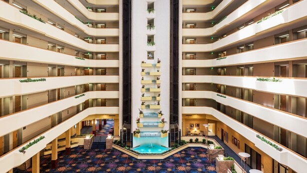 Un atrium d’hôtel à plusieurs niveaux, doté d’un élément aquatique central, de balcons ornés de plantes et d’un tapis à motifs.