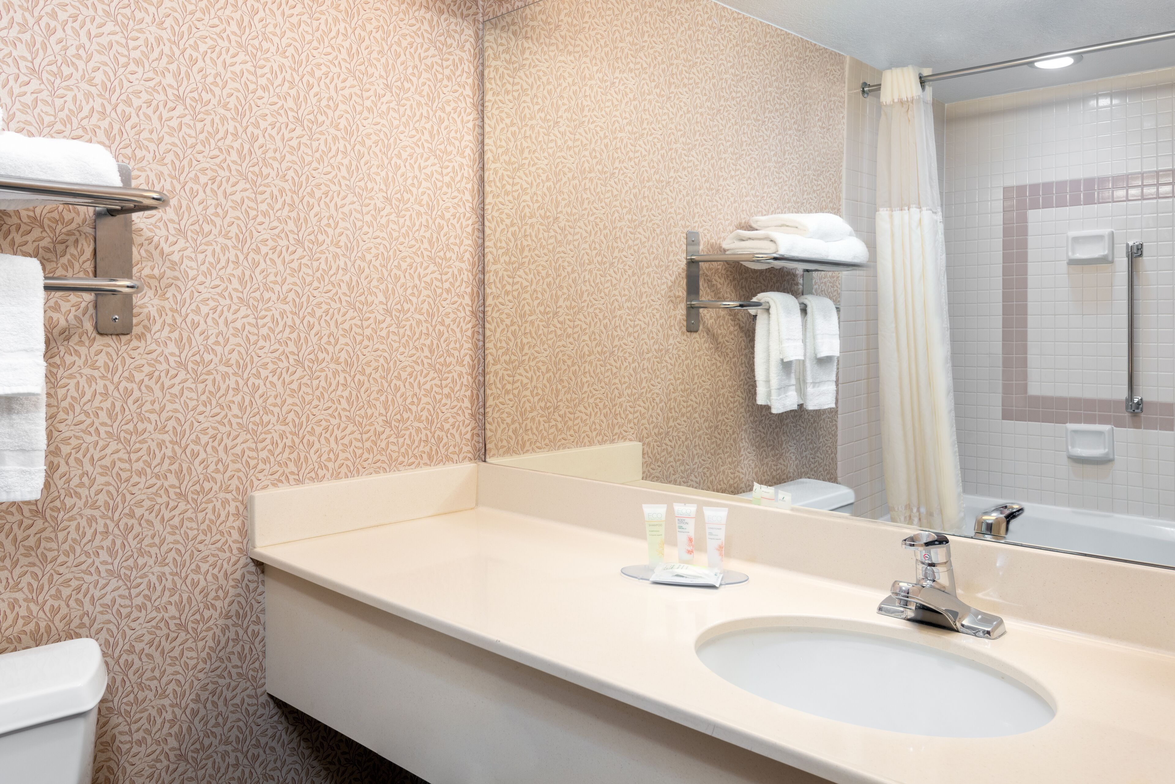 A bathroom with a patterned wall, a sink with a mirror, and a shower area.