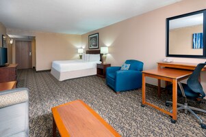 Habitación de hotel con cama, escritorio, sillón, sofá y televisión.