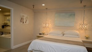 A bedroom with a large bed, two bedside tables, a nightstand, a wall-mounted artwork, and a hanging light fixture. - Hotel Le Rêve Pasadena (Pasadena)