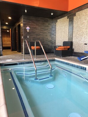 Una piscina con una escalera de metal, un banco y una pared con un diseño texturizado.