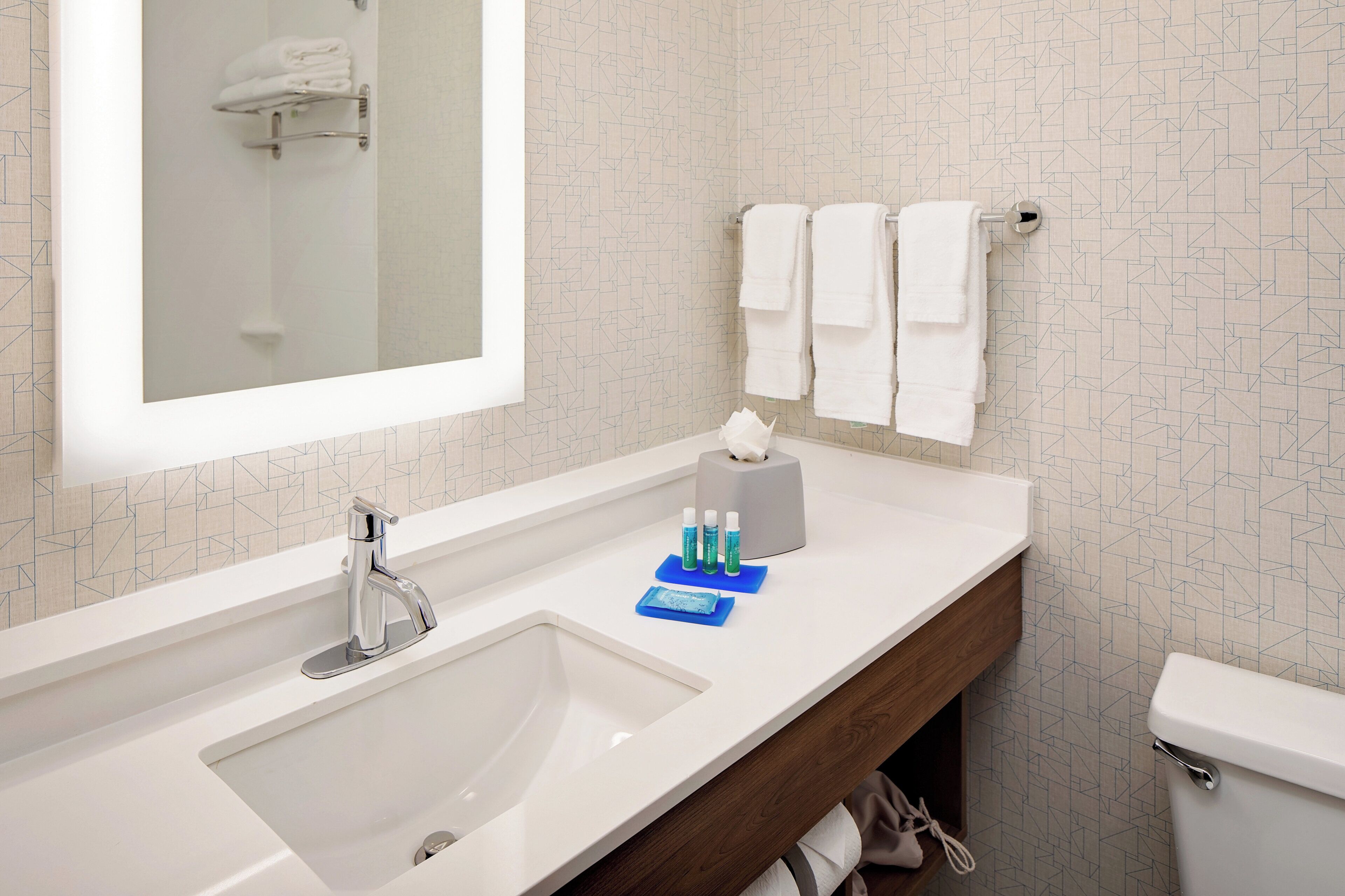 Ein Badezimmer mit weißem Waschbecken, einem Spiegel, einem Handtuchhalter und Toilettenartikeln.