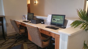 Un espacio de trabajo en un hotel con dos computadoras, una impresora y dos sillas de oficina.