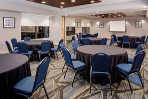 A conference room with round tables and blue chairs, carpeted floor, and a projector screen. - Holiday Inn Express - Harrisburg East by IHG (Harrisburg)