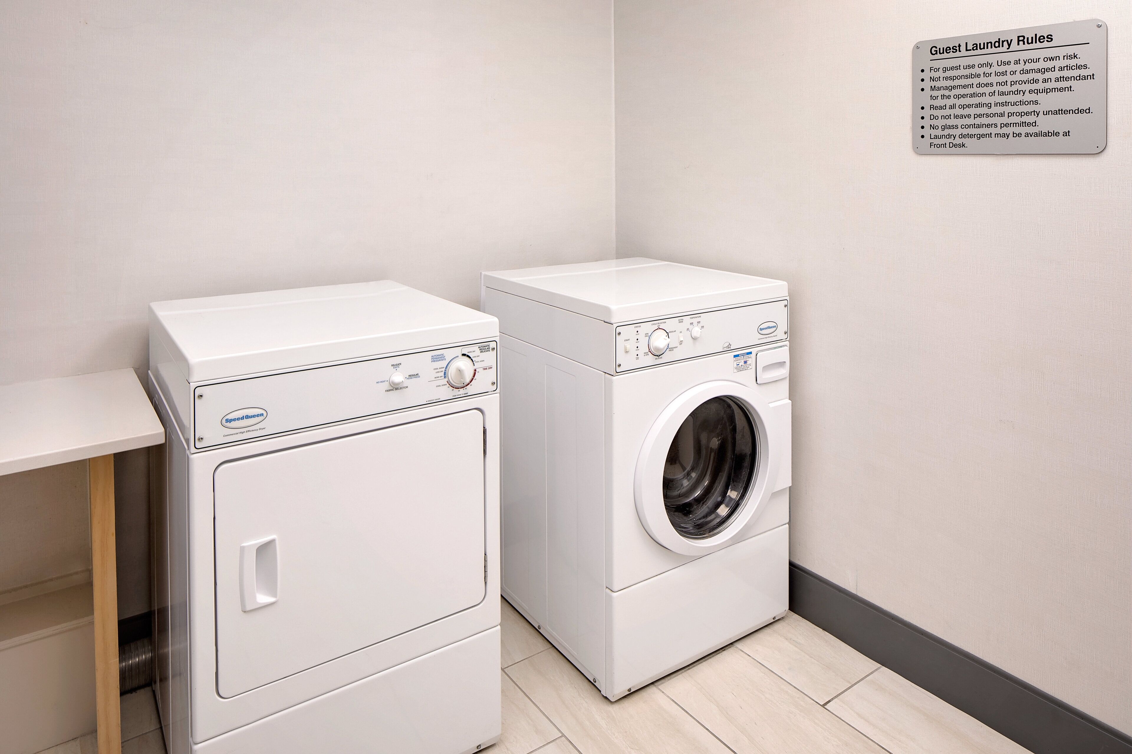 Une buanderie équipée de deux machines à laver à chargement frontal, toutes deux de couleur blanche, et d’un panneau indiquant les règles à respecter pour l’utilisation de la buanderie par les clients.