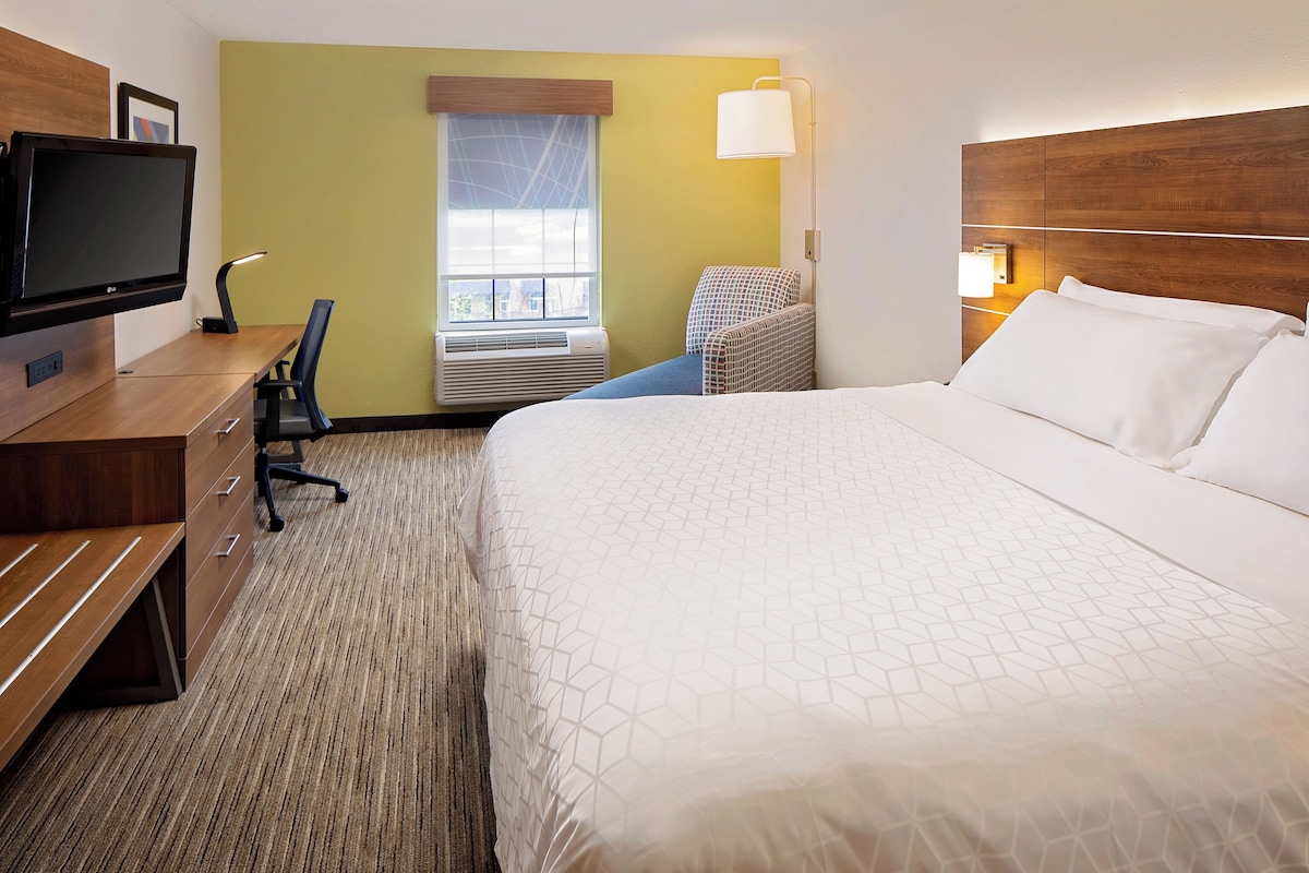 Habitación de hotel con cama, escritorio, silla, televisor y ventana con persianas.