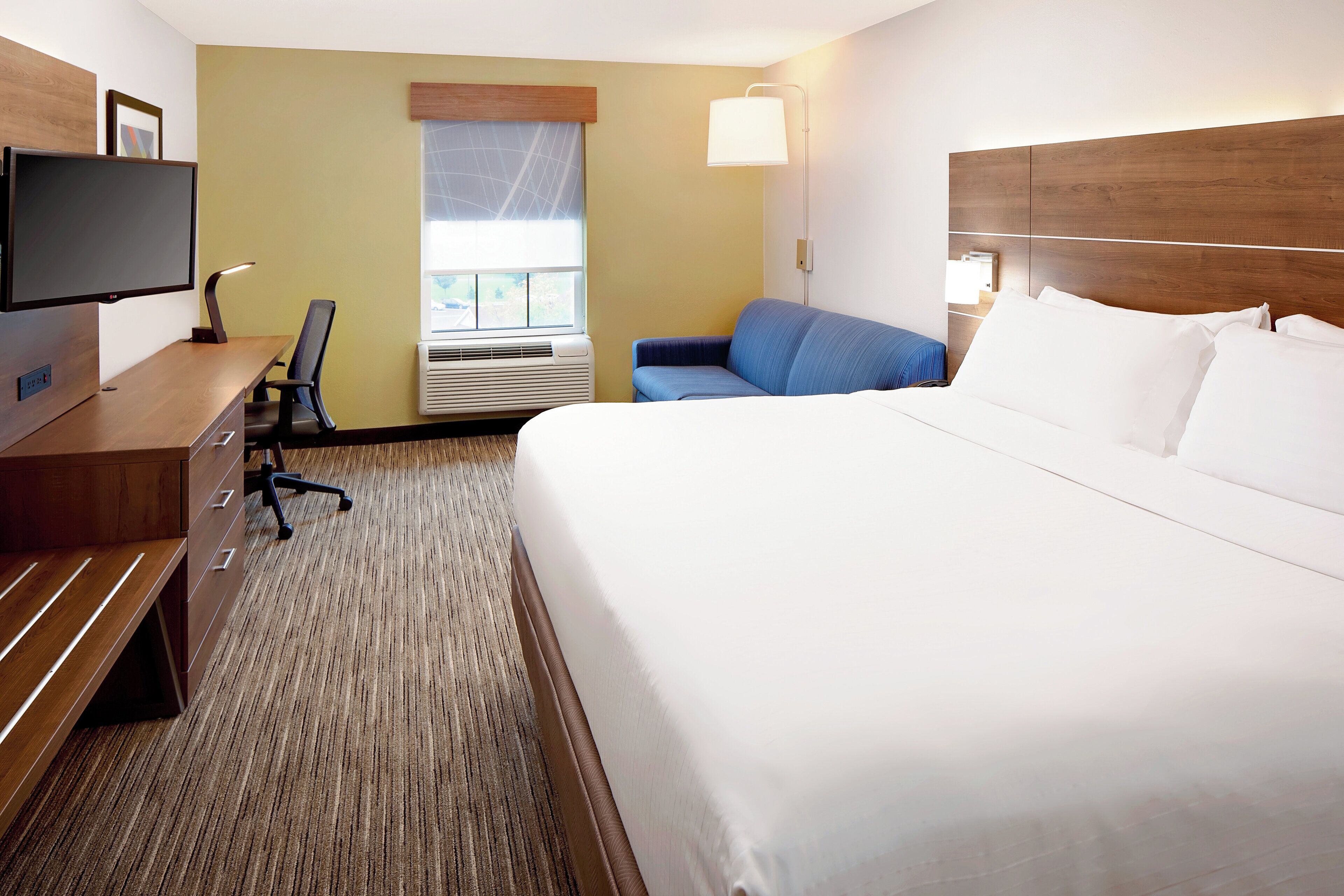 A hotel room with a bed, a desk, a chair, a TV, and a window.