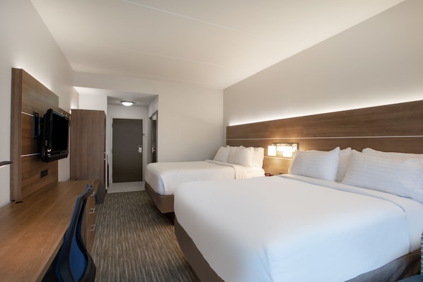 Habitación de hotel con dos camas, un escritorio, un televisor y una puerta que da a otra habitación.