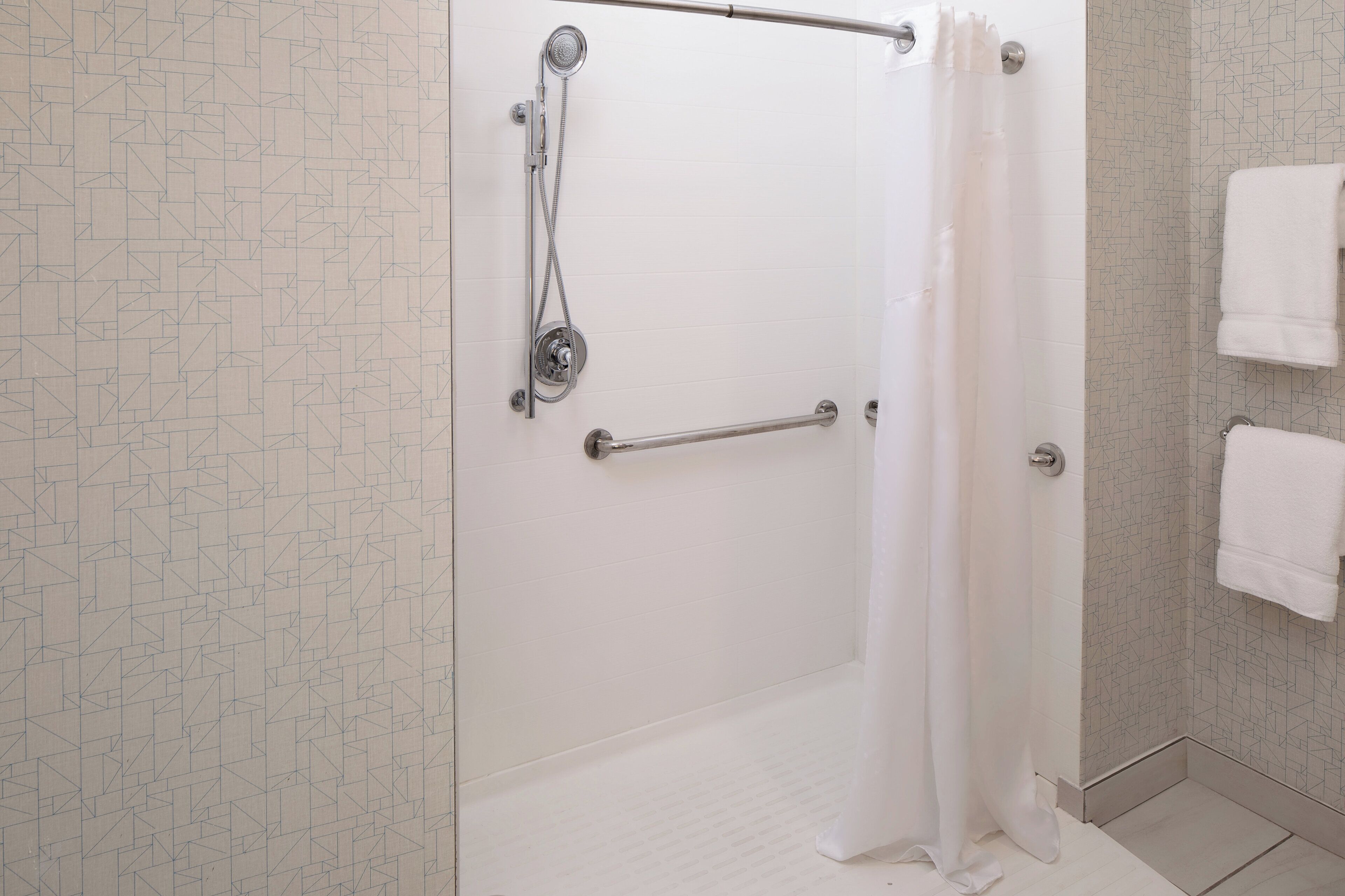 Un baño con ducha, barra de apoyo y paredes de azulejos blancos.