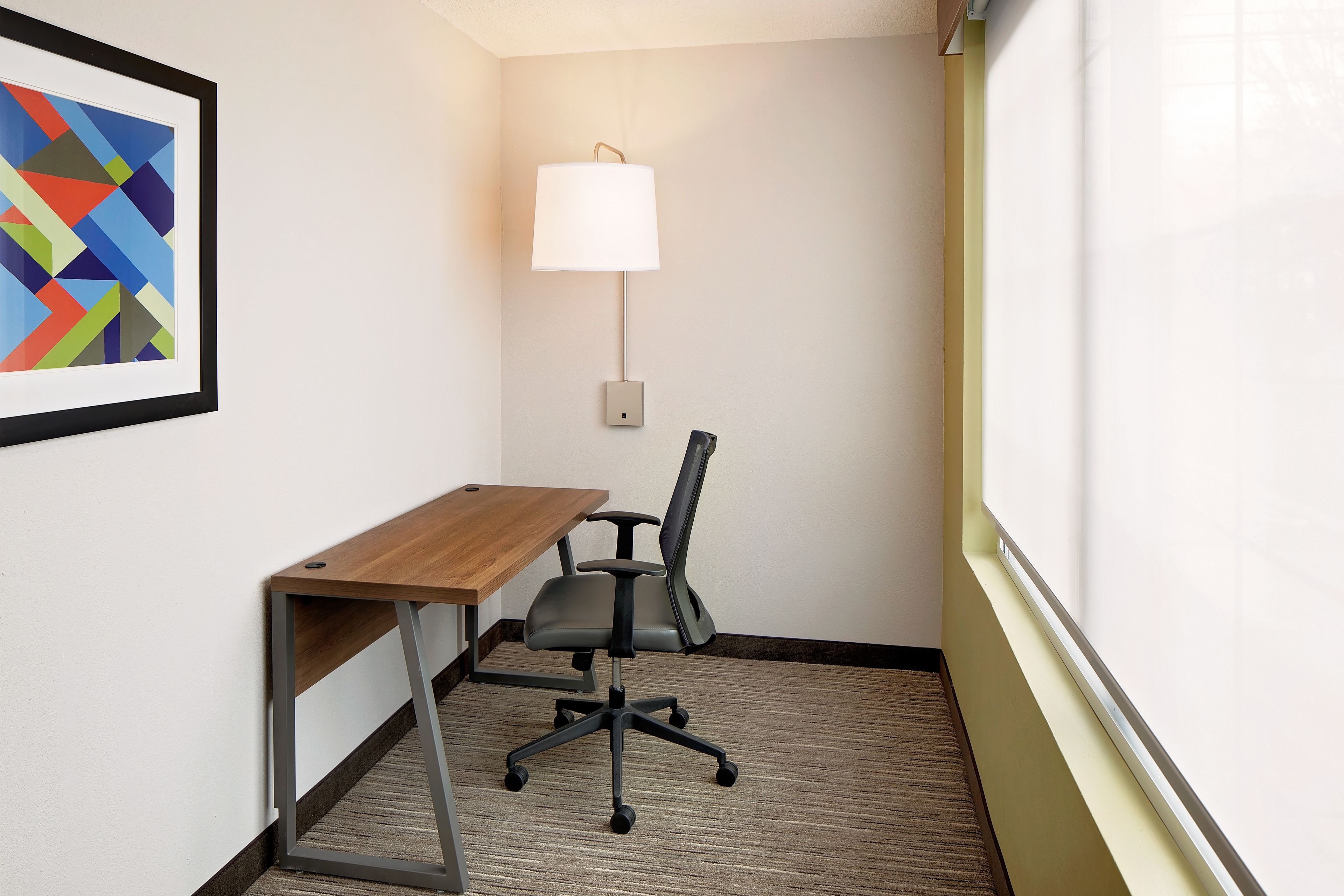 A small office space with a desk, office chair, and a wall-mounted lamp.
