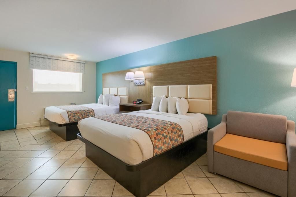 Habitación de hotel con dos camas, un sofá, una ventana y un televisor instalado en la pared.