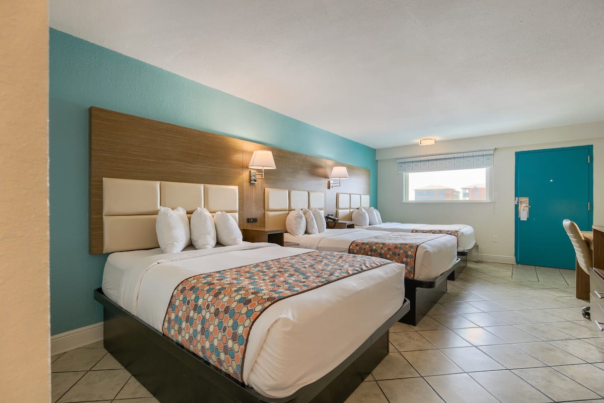 A hotel room with two beds, a wooden headboard, a window with blinds, and a teal-colored wall.