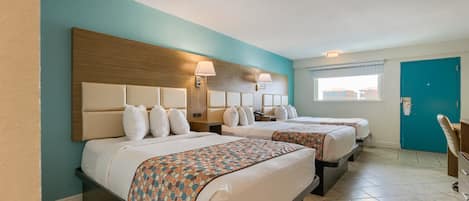 A hotel room with two beds, a wooden headboard, a window with blinds, and a teal-colored wall.