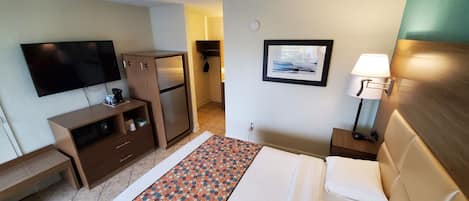 Una habitación de hotel con cama, televisión, escritorio, armario y un cuadro en la pared.