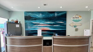 A reception area with two wooden reception desks, a large abstract painting on the wall, and a 'BEACH' sign.
