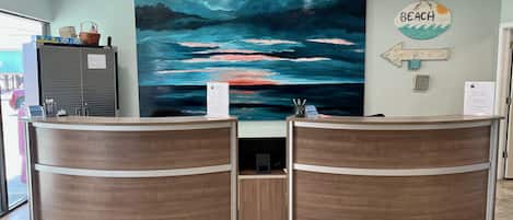 Ett entrérum med två receptioner i trä, en stor abstrakt målning på väggen och en skylt med texten ”BEACH”.