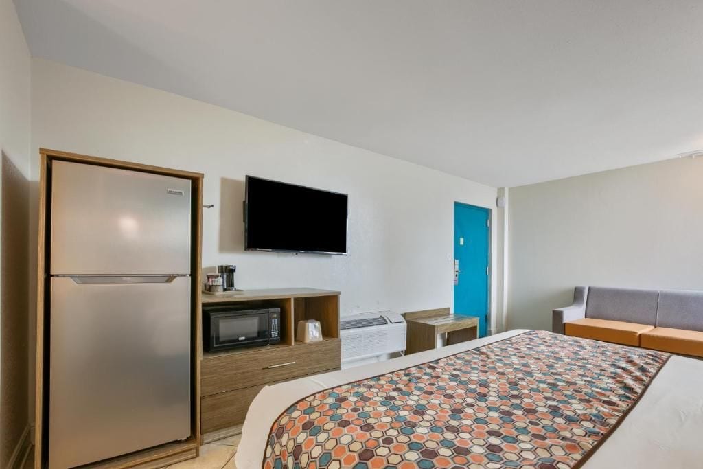 Habitación de hotel con cama, televisor, microondas, refrigerador, escritorio y una puerta azul.