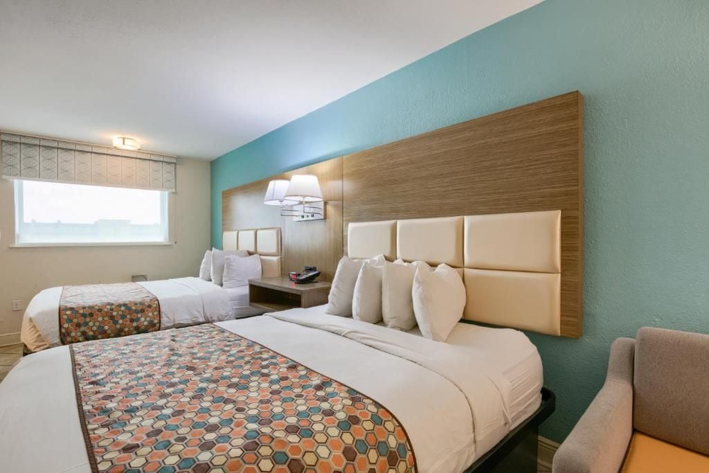 A hotel room with two beds, a large window, a wall-mounted lamp, and a headboard.
