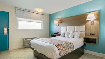 A modern hotel room with a large bed, a window with blinds, a wall-mounted lamp, and a built-in shelf.