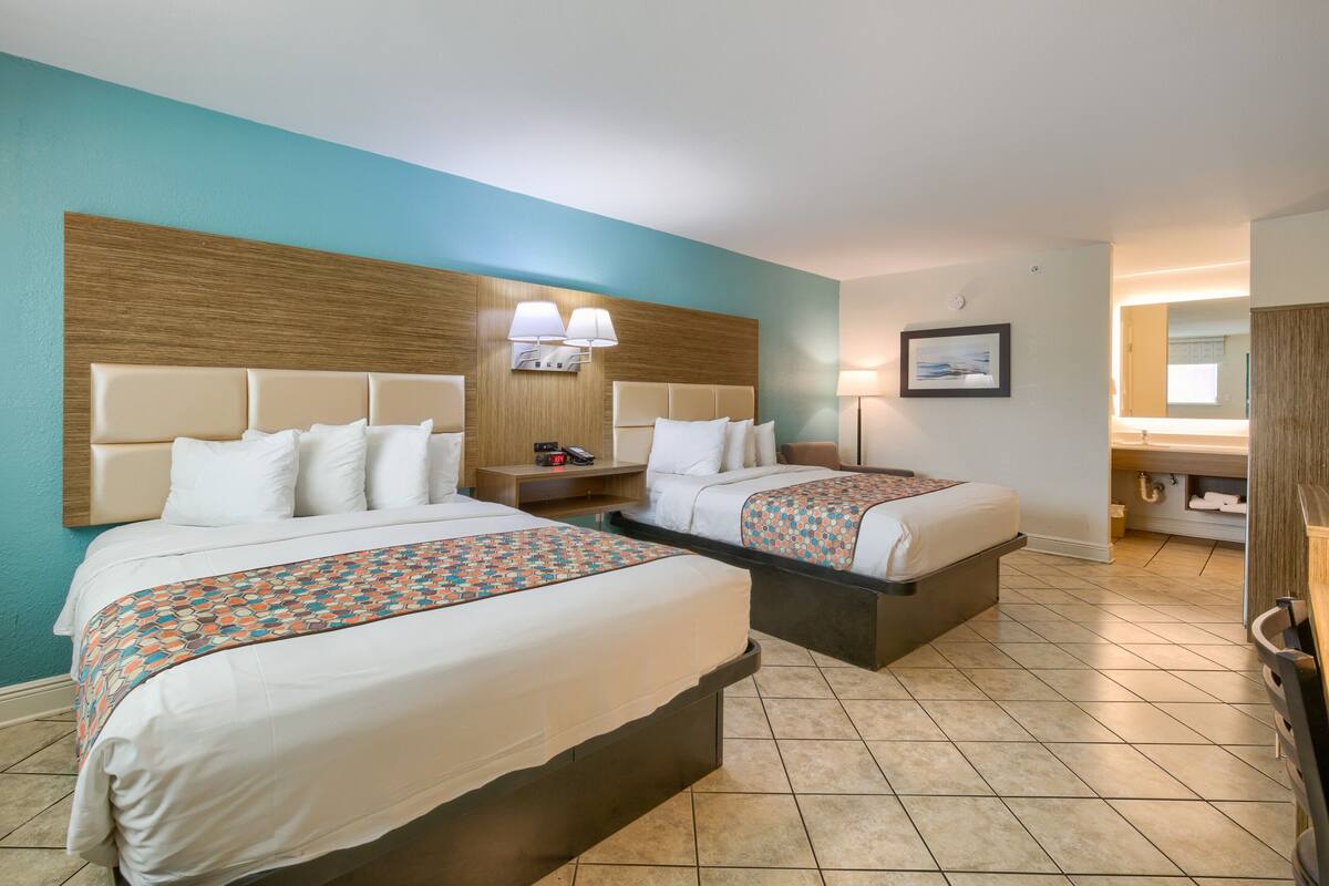 A hotel room with two beds, a wooden headboard, a nightstand, and a wall-mounted lamp.