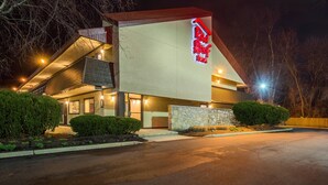 Un hotel Red Roof Inn con diseño moderno, que cuenta con un llamativo letrero rojo y blanco, fachada de piedra y estacionamiento.