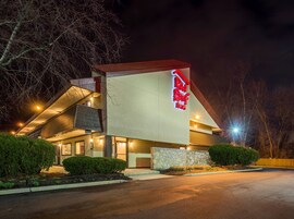 Un hotel Red Roof Inn con diseño moderno, que cuenta con un llamativo letrero rojo y blanco, fachada de piedra y estacionamiento.