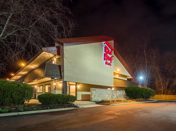 Un hotel Red Roof Inn con diseño moderno, que cuenta con un llamativo letrero rojo y blanco, fachada de piedra y estacionamiento.