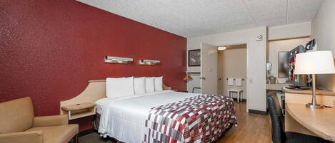 A hotel room with a bed, a desk, a chair, a desk lamp, and a television.