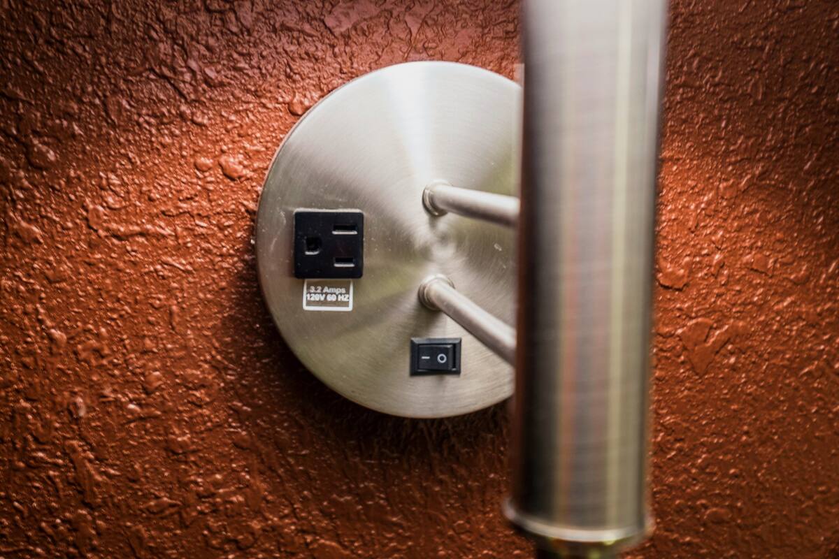 A metallic, circular object with two electrical outlets and a switch, mounted on a textured wall.