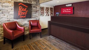 Zona de recepción de Red Roof Inn con dos sillones de cuero, pared de piedra y un cartel que indica Wi-Fi gratuito en todas las habitaciones.