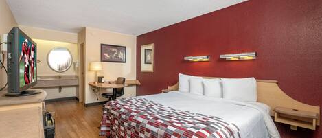 A hotel room with a bed, a desk, a television, a mirror, and two wall-mounted lights.