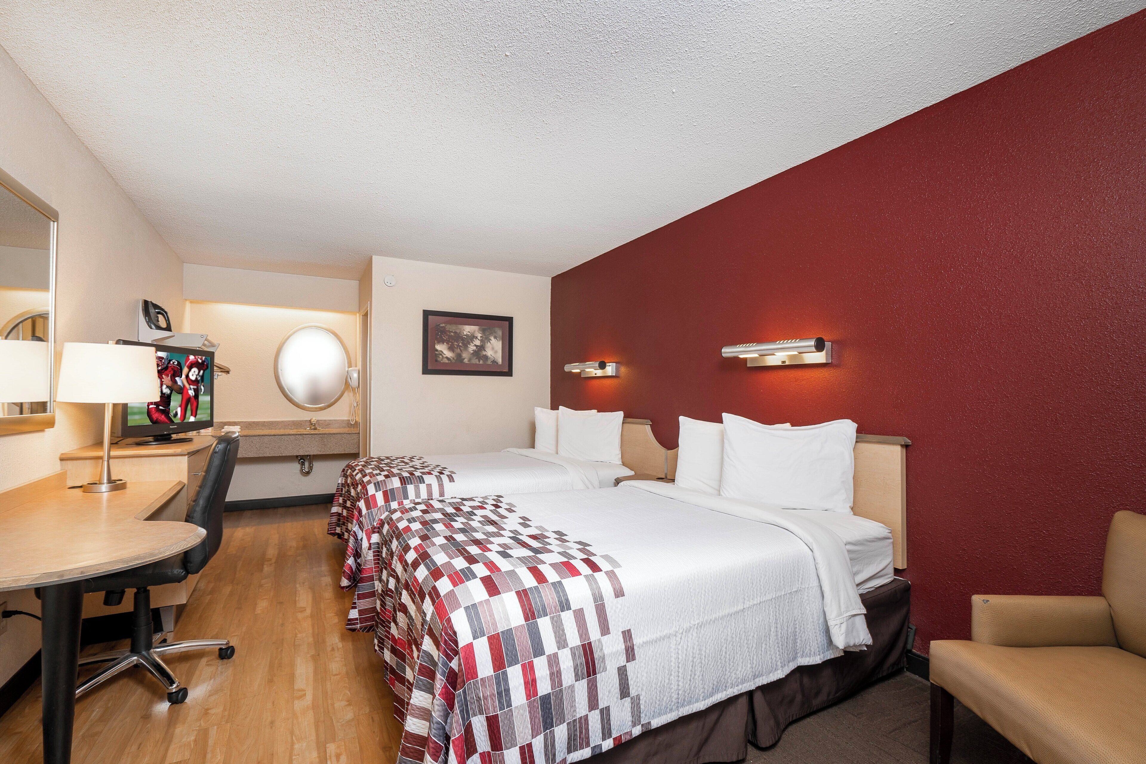 Ein Hotelzimmer mit Bett, Schreibtisch, Stuhl, Fernseher und einer roten Akzentwand.