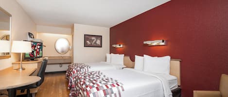 Une chambre d’hôtel avec un lit, un bureau, une chaise, une télévision et un mur d’accent rouge.
