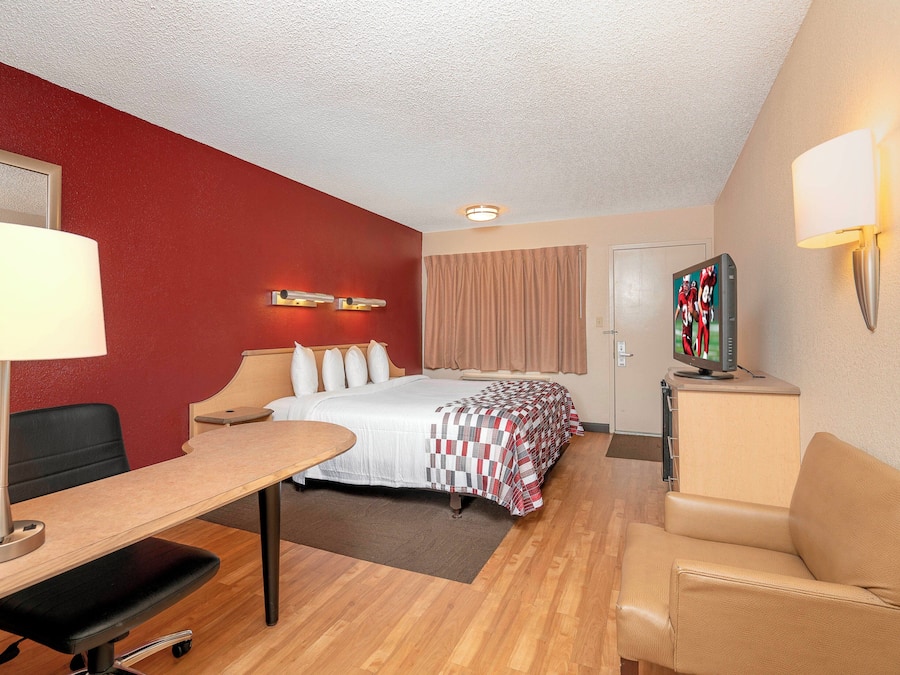 A hotel room with a bed, desk, chair, lamp, television, and a door.