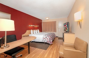 Habitación de hotel con cama, escritorio, silla, lámpara, televisor y puerta.