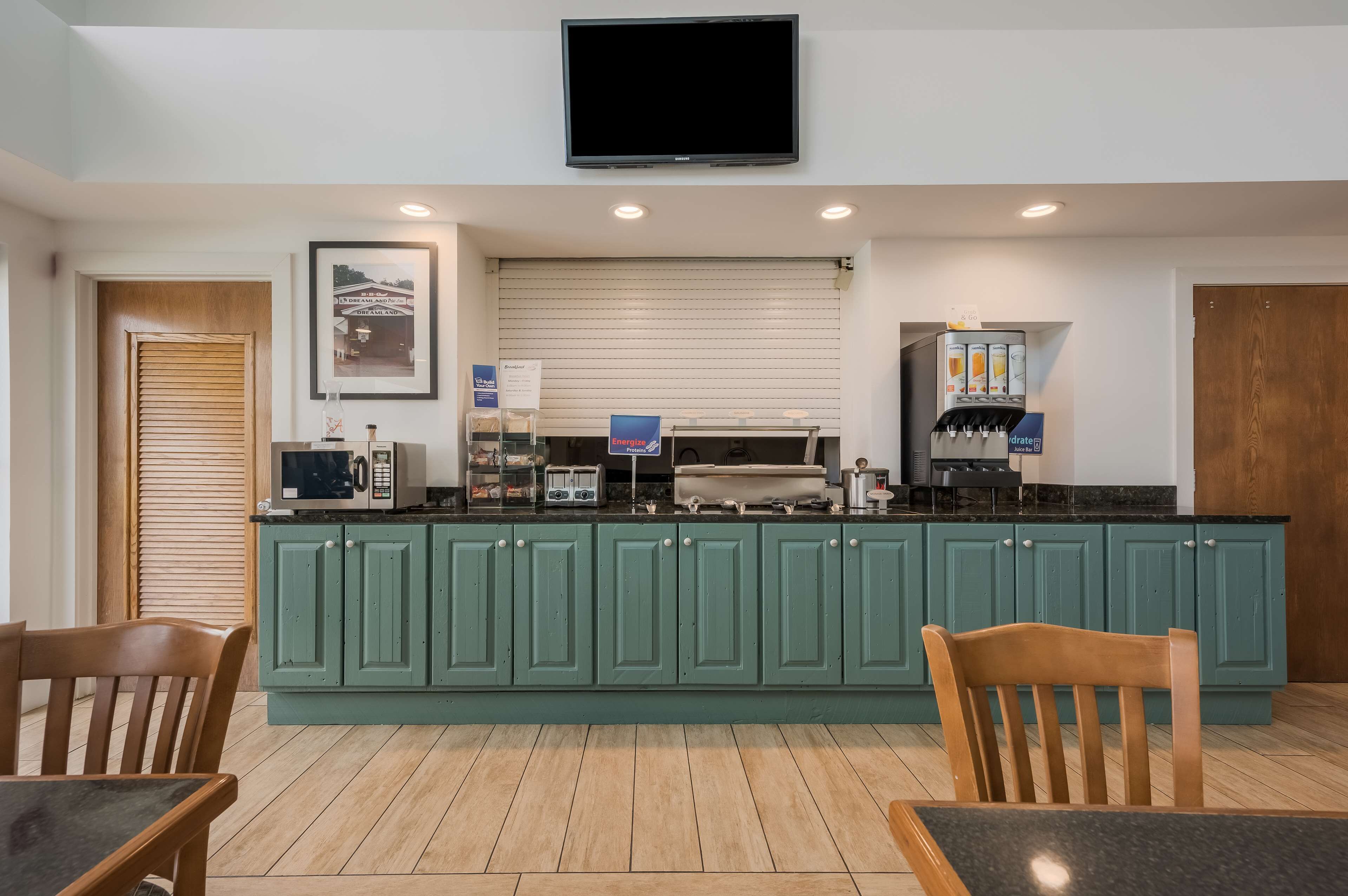Una cocina moderna con armarios verdes, un microondas, una cafetera y un televisor de pantalla plana montado en la pared.