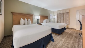 A hotel room with two beds, a wooden headboard, a lamp, a telephone, and a door with a mirror.