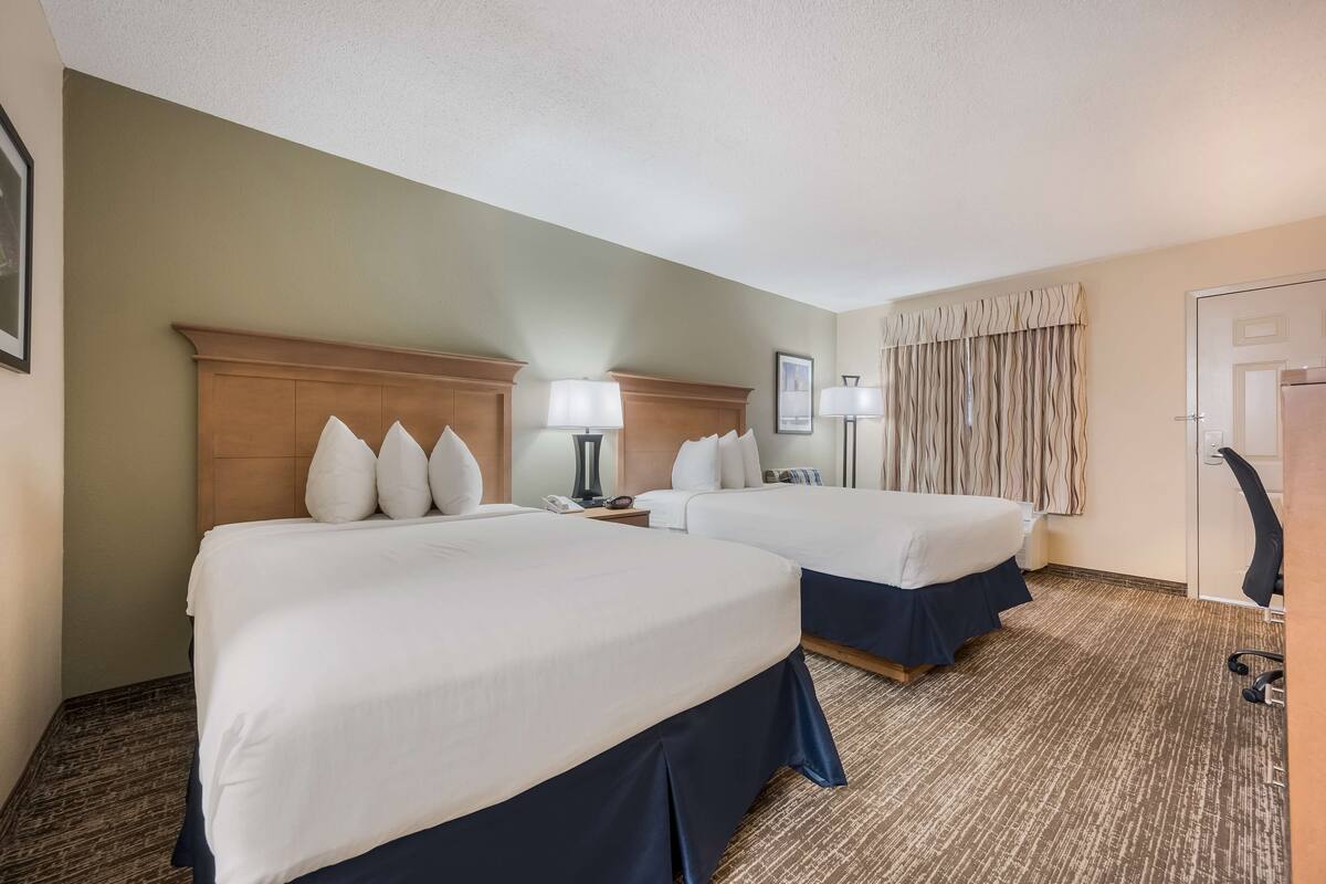 A hotel room with two beds, a wooden headboard, a lamp, a telephone, and a door with a mirror.
