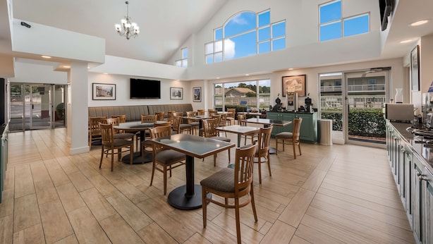 A spacious dining area with multiple tables and chairs, a kitchen area with a bar, and large windows providing natural light.