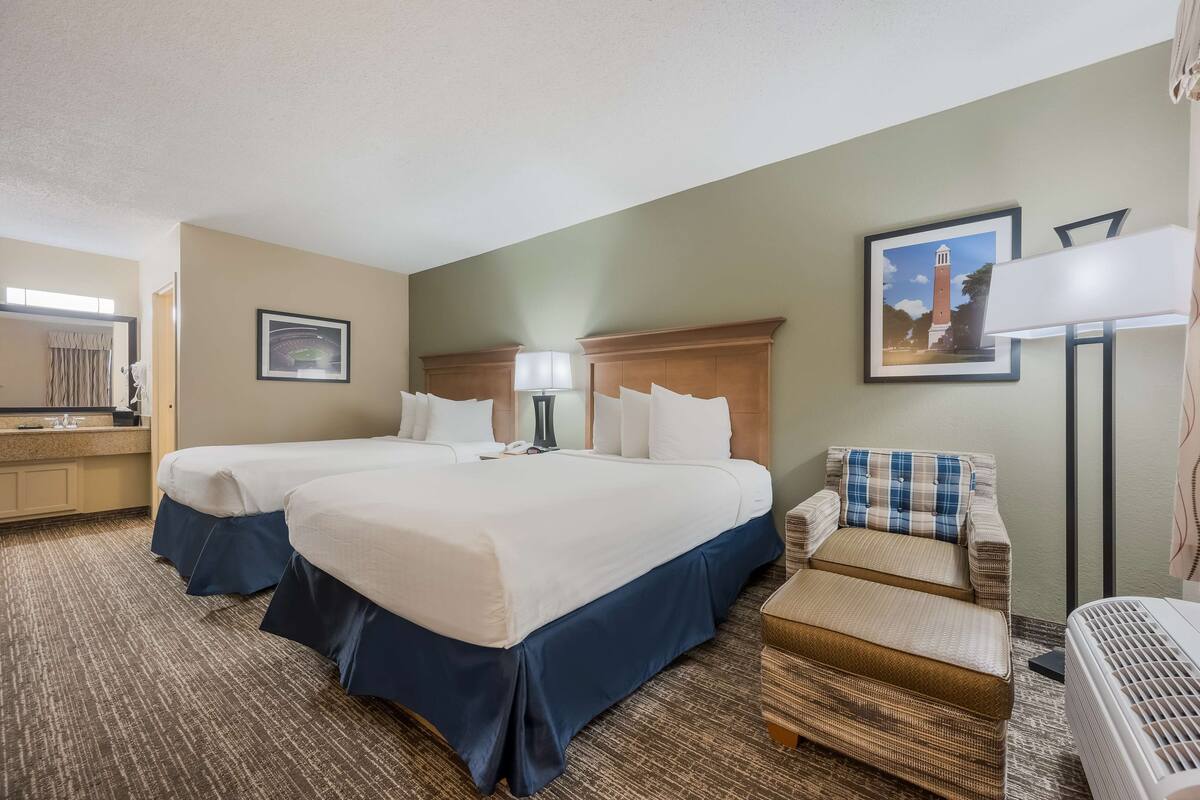 A hotel room with two beds, a desk with a lamp, a chair, and a picture on the wall.