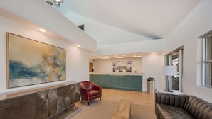 A modern interior with a large abstract painting, a leather armchair, a brown leather sofa, and a kitchen area in the background.