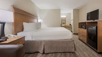A hotel room with a bed, a desk with a phone and a clock, a TV, a microwave, and a refrigerator.