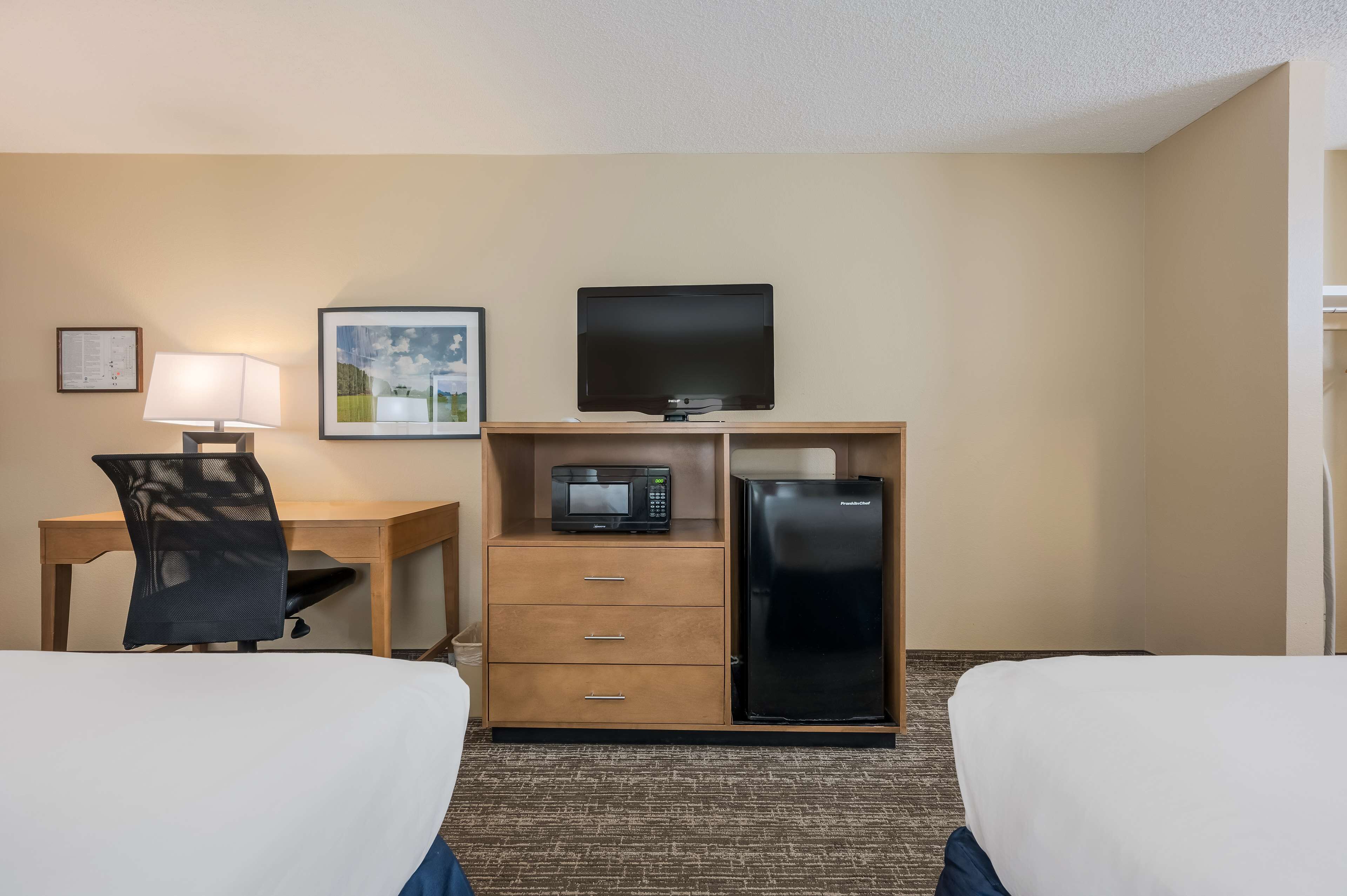 A hotel room with two beds, a desk with a lamp, a television, a microwave, and a refrigerator.