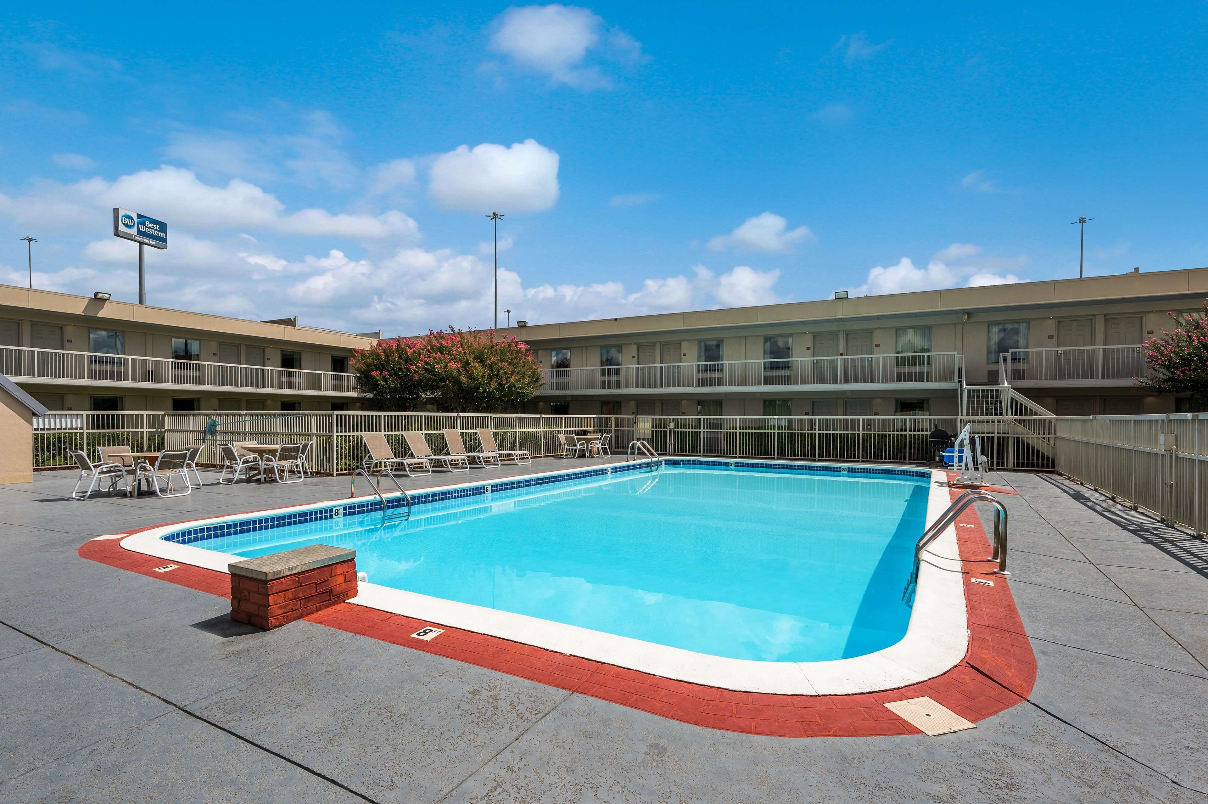 A swimming pool with a red and white edge, surrounded by a fence and a building with a sign that reads "B&B".